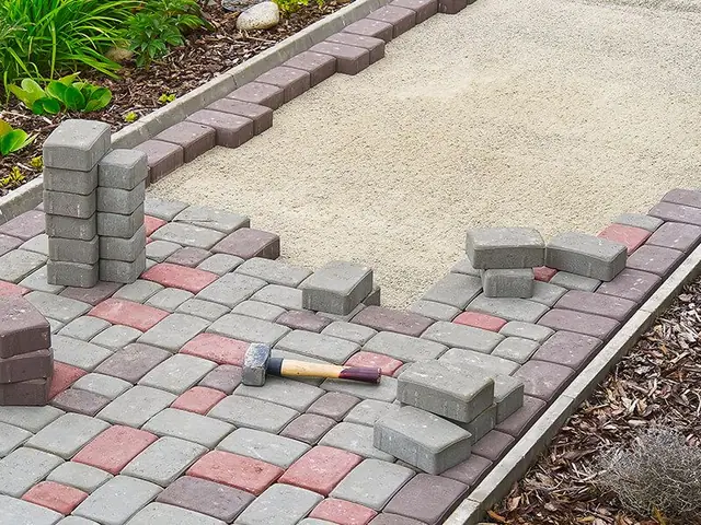 A hammer is laying on top of a brick walkway being built.