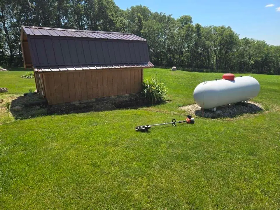 A propane tank is sitting in the grass next to a shed.